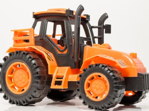Een gele Bruder-tractor van geel plastic op een houten vloer, zoals kinderen die speelden in de jaren 80