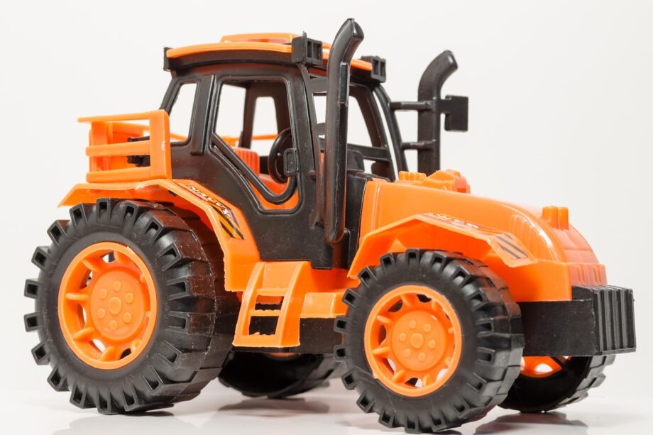 Een gele Bruder-tractor van geel plastic op een houten vloer, zoals kinderen die speelden in de jaren 80