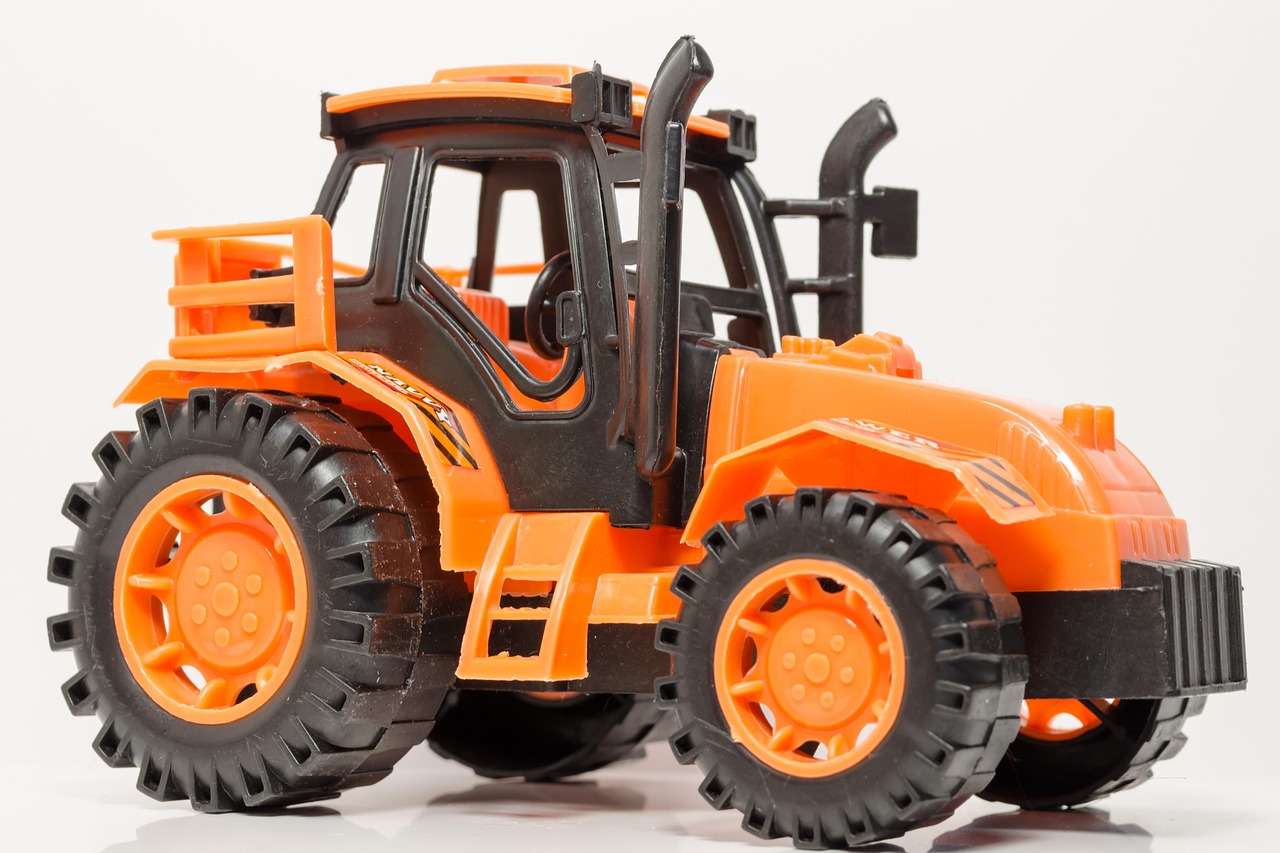 Een gele Bruder-tractor van geel plastic op een houten vloer, zoals kinderen die speelden in de jaren 80