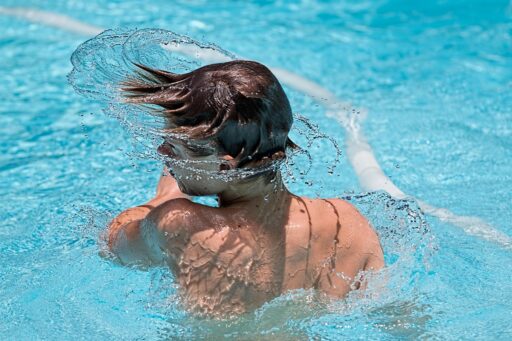 Een zonnig buitenzwembad met blauwe tegels en kinderen die spelen in het water