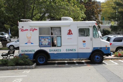 Een klassieke ijscowagen geparkeerd in een Nederlandse woonstraat op een zomerse dag