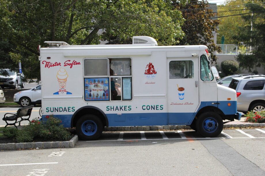 Een klassieke ijscowagen geparkeerd in een Nederlandse woonstraat op een zomerse dag