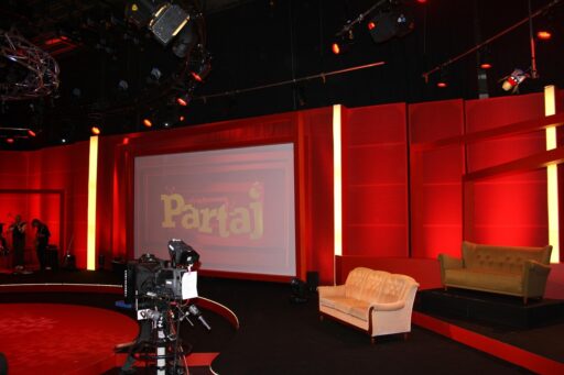Een jonge vrouw staat voor een televisiecamera in een typische jaren 80 televisiestudio